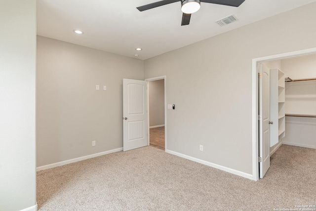 unfurnished bedroom featuring a walk in closet, light carpet, a closet, and ceiling fan