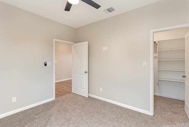 unfurnished bedroom with a walk in closet, a closet, ceiling fan, and carpet floors