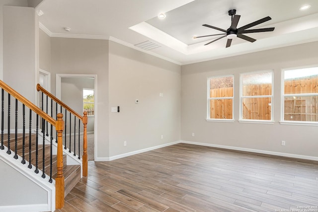 empty room with ceiling fan, crown molding, hardwood / wood-style flooring, and a tray ceiling