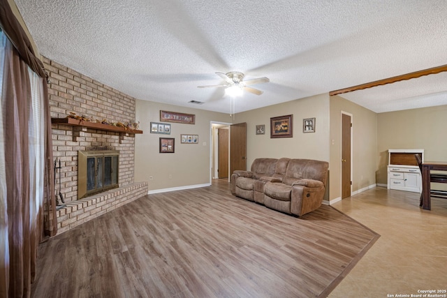 living room with a fireplace, a textured ceiling, ceiling fan, and light hardwood / wood-style flooring