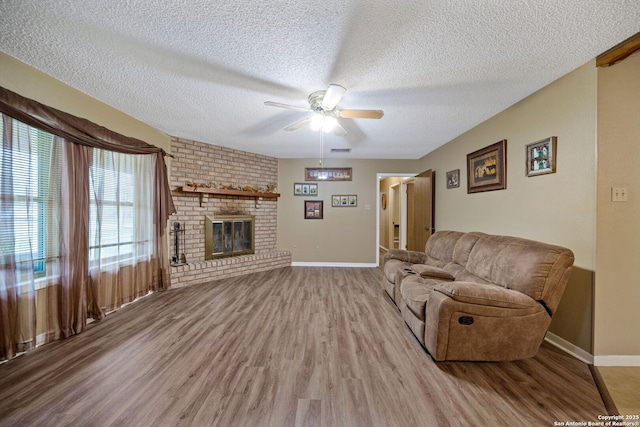 living room with light wood-type flooring, a fireplace, a textured ceiling, and ceiling fan