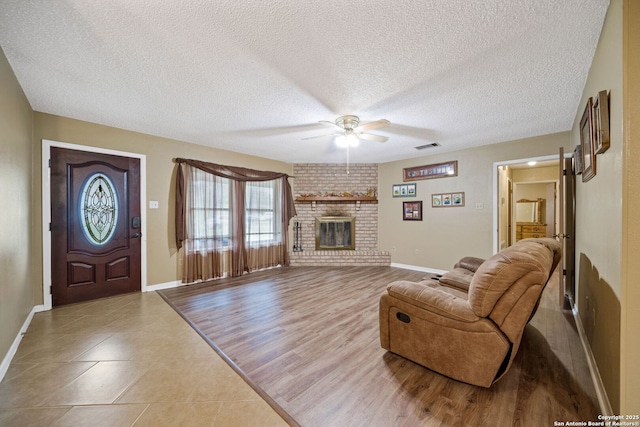 tiled living room featuring a brick fireplace, a textured ceiling, and ceiling fan