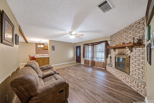 living room with brick wall, ceiling fan, a fireplace, a textured ceiling, and light hardwood / wood-style flooring