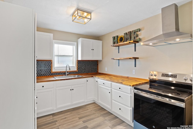 kitchen featuring sink, white cabinetry, wall chimney exhaust hood, stainless steel electric range, and butcher block countertops