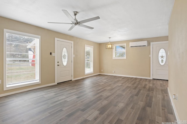 foyer entrance featuring ceiling fan with notable chandelier, dark wood-type flooring, an AC wall unit, and a wealth of natural light