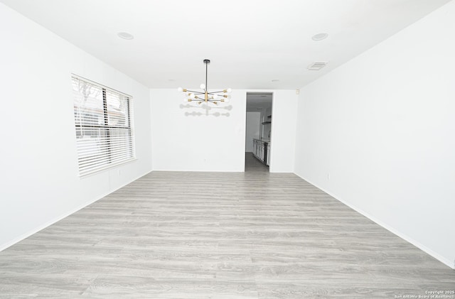 empty room with an inviting chandelier and light hardwood / wood-style floors