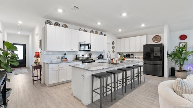 kitchen with white cabinets, stainless steel appliances, a center island with sink, and a kitchen breakfast bar