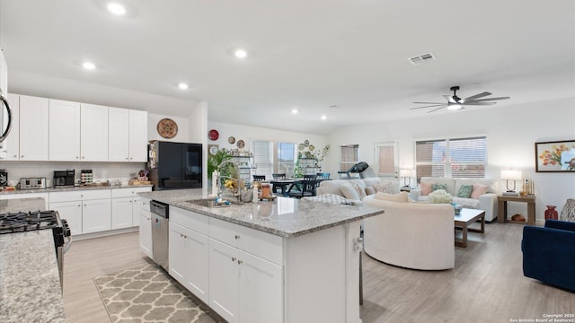 kitchen featuring light stone countertops, stainless steel appliances, a center island with sink, backsplash, and white cabinetry