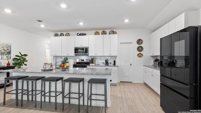 kitchen featuring stainless steel appliances, light stone countertops, white cabinets, and an island with sink