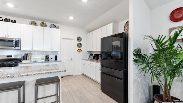 kitchen with stainless steel appliances, white cabinetry, light stone counters, tasteful backsplash, and a breakfast bar