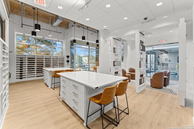 kitchen with white cabinets, a drop ceiling, light wood-type flooring, a kitchen island, and pendant lighting