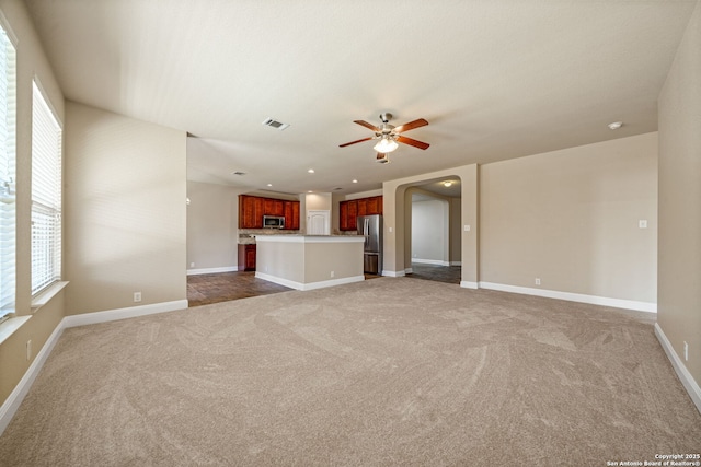 unfurnished living room featuring ceiling fan, a wealth of natural light, and dark colored carpet