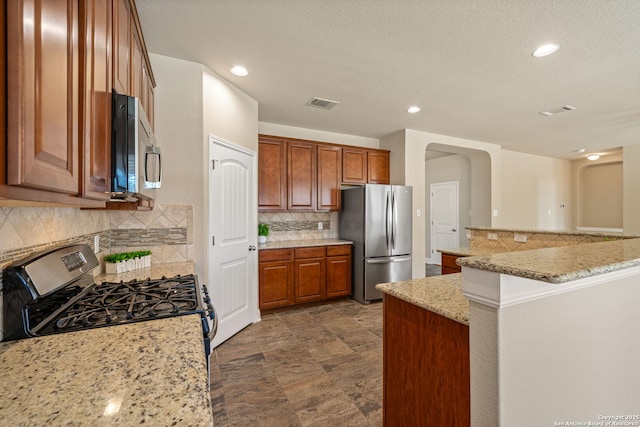 kitchen with light stone counters, kitchen peninsula, a breakfast bar area, backsplash, and appliances with stainless steel finishes