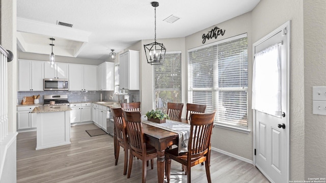 dining area with sink, a tray ceiling, light hardwood / wood-style floors, and a notable chandelier