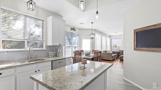 kitchen with a center island, sink, white cabinetry, stainless steel dishwasher, and backsplash