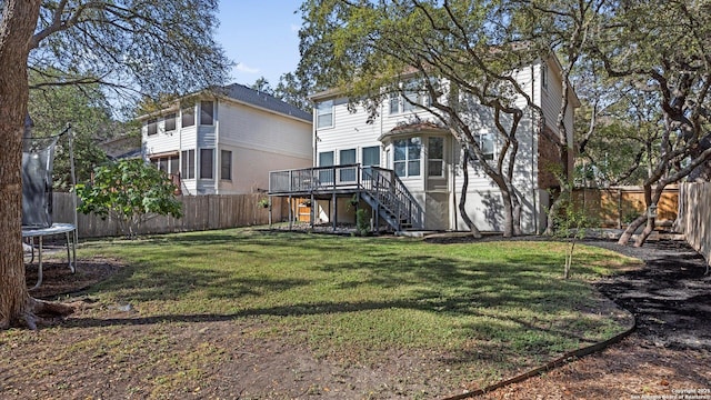 back of house featuring a deck, a yard, and a trampoline