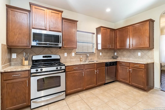 kitchen featuring stainless steel appliances, decorative backsplash, sink, and light stone countertops