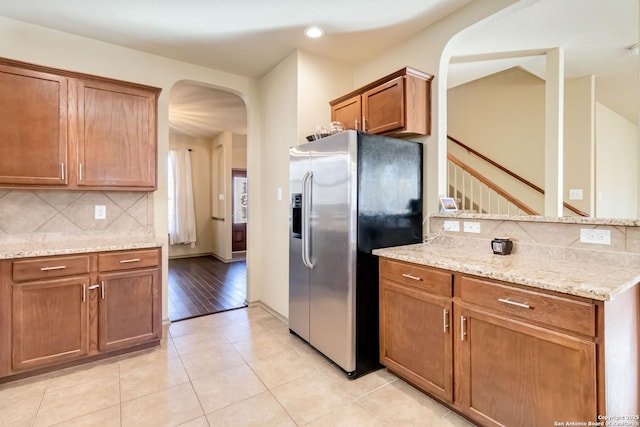 kitchen with light stone countertops, stainless steel fridge, light tile patterned floors, and tasteful backsplash