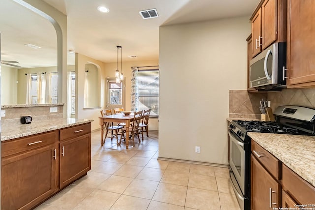 kitchen with stainless steel appliances, light stone countertops, decorative light fixtures, light tile patterned flooring, and tasteful backsplash