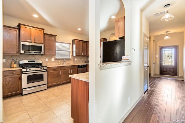 kitchen featuring light stone counters, pendant lighting, stainless steel appliances, tasteful backsplash, and sink