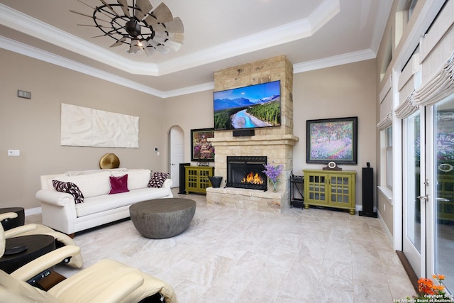 living room featuring ceiling fan, crown molding, a stone fireplace, and a raised ceiling