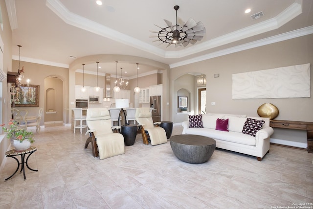 living room with ceiling fan with notable chandelier, a raised ceiling, and ornamental molding