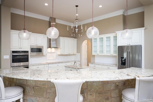 kitchen featuring wall chimney exhaust hood, stainless steel appliances, white cabinetry, and pendant lighting