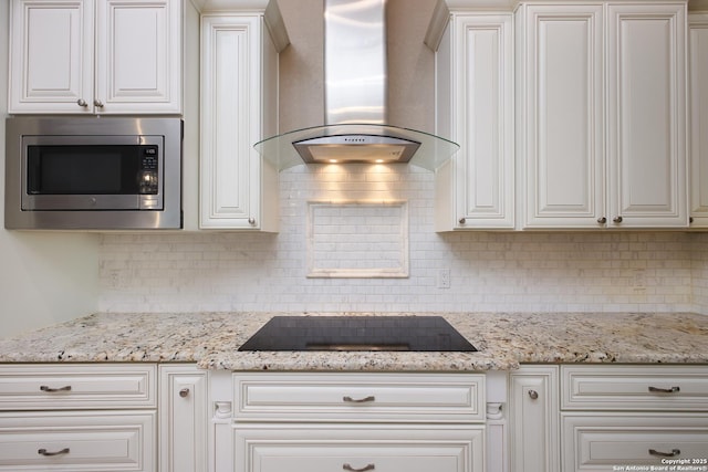 kitchen featuring black electric stovetop, light stone countertops, wall chimney exhaust hood, stainless steel microwave, and tasteful backsplash