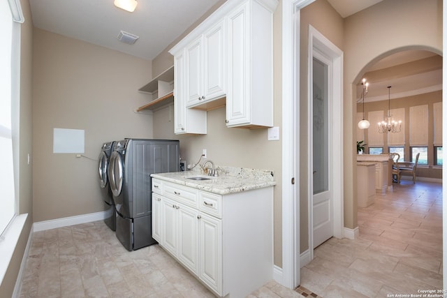 laundry area featuring washer and dryer, an inviting chandelier, sink, and cabinets