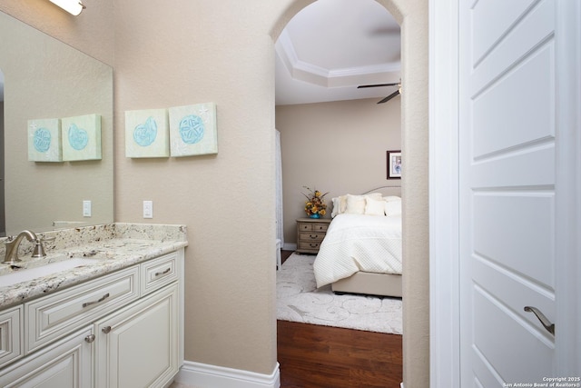 bathroom featuring a raised ceiling, ceiling fan, wood-type flooring, vanity, and crown molding