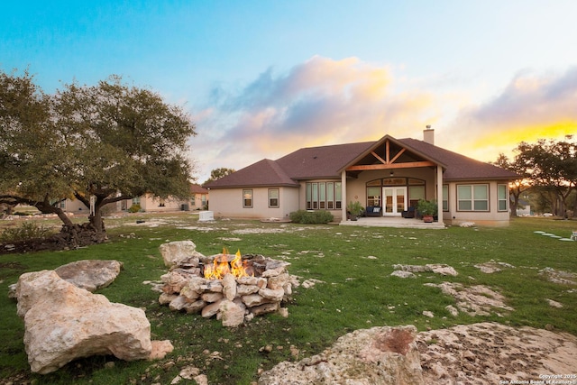 back house at dusk featuring a fire pit, a yard, and a patio