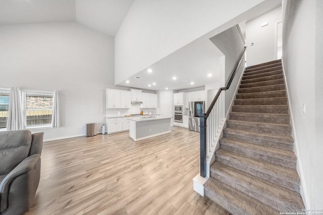 staircase featuring sink, high vaulted ceiling, and hardwood / wood-style flooring