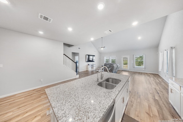 kitchen featuring white cabinets, a kitchen island with sink, light stone countertops, and sink