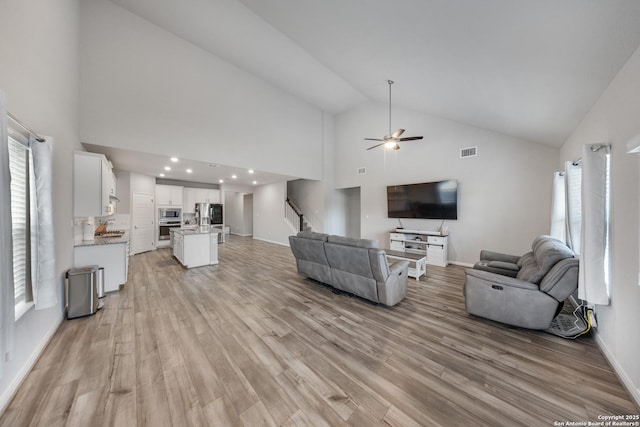 living room with high vaulted ceiling, ceiling fan, and light hardwood / wood-style flooring