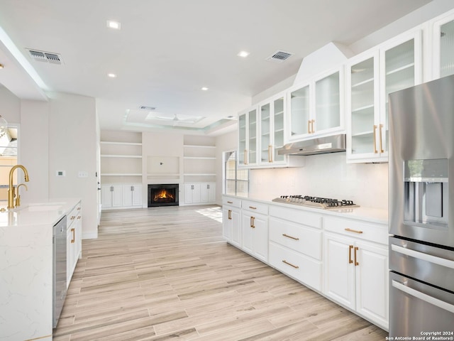 kitchen with light stone countertops, light wood-type flooring, white cabinetry, appliances with stainless steel finishes, and sink