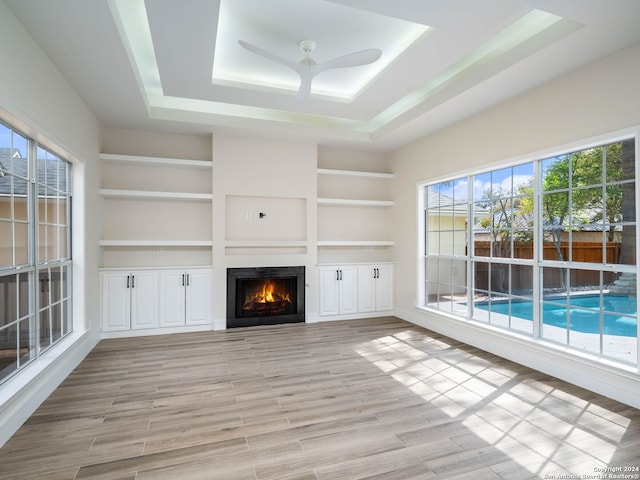 unfurnished living room featuring ceiling fan, built in features, and a tray ceiling