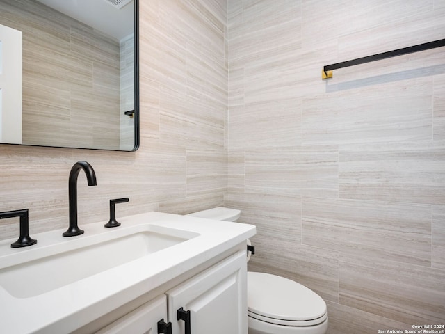 bathroom with toilet, vanity, decorative backsplash, and tile walls