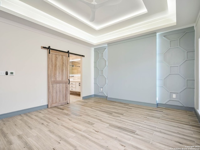 empty room featuring light hardwood / wood-style flooring, a raised ceiling, and a barn door