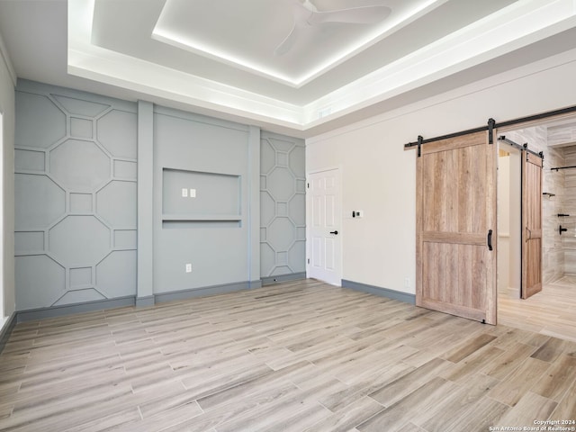 unfurnished bedroom with ceiling fan, a tray ceiling, and a barn door