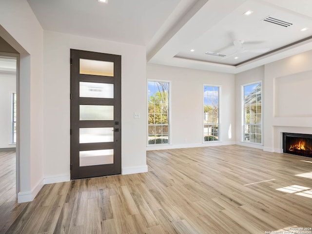 foyer with ceiling fan, a wealth of natural light, light wood-type flooring, and a tray ceiling