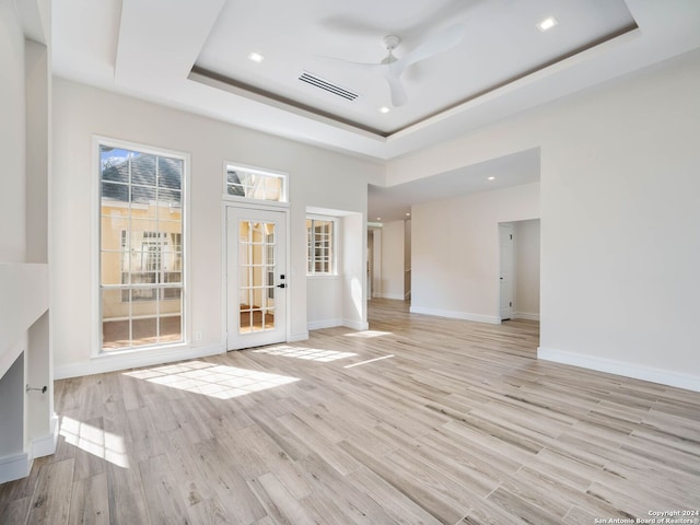 unfurnished living room featuring ceiling fan, light hardwood / wood-style flooring, and a tray ceiling