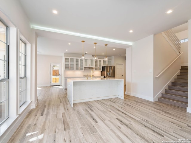 kitchen featuring light wood-type flooring, a large island with sink, pendant lighting, high quality fridge, and white cabinetry