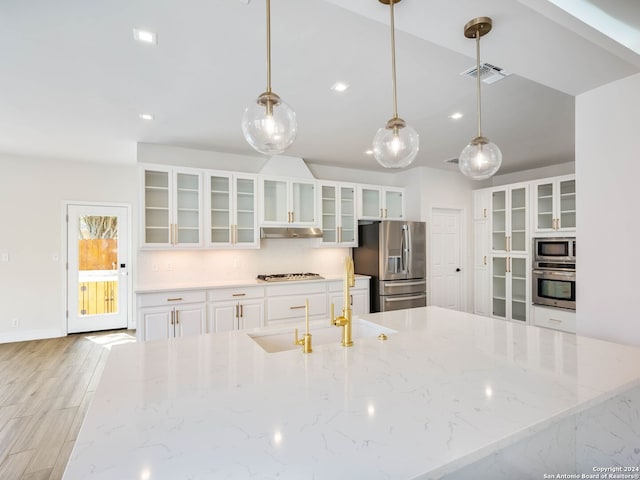 kitchen with light stone counters, hanging light fixtures, white cabinets, appliances with stainless steel finishes, and sink