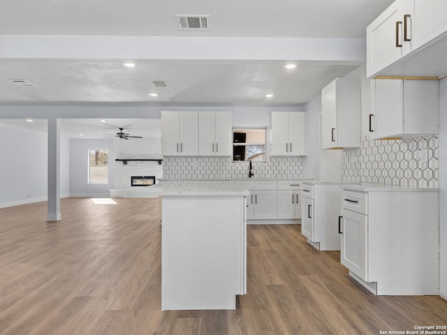 kitchen with white cabinets, a fireplace, ceiling fan, light wood-type flooring, and a kitchen island