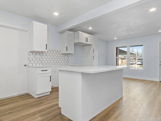 kitchen with light stone countertops, light hardwood / wood-style flooring, a center island, decorative backsplash, and white cabinetry