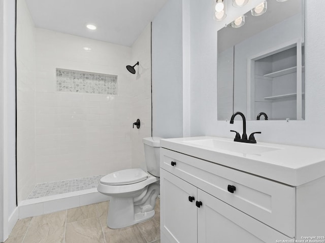 bathroom with a tile shower, vanity, and toilet