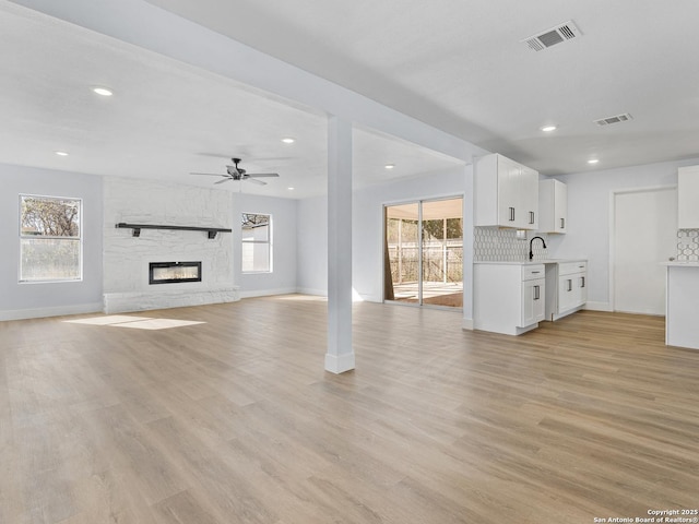 unfurnished living room featuring a healthy amount of sunlight, ceiling fan, light hardwood / wood-style floors, and a stone fireplace