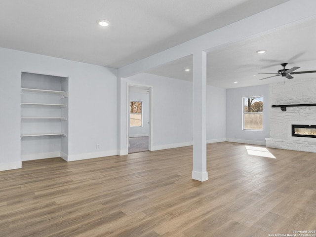 unfurnished living room featuring ceiling fan, light hardwood / wood-style floors, built in features, and a fireplace