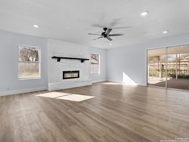 unfurnished living room with a fireplace, ceiling fan, and light wood-type flooring