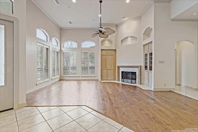 unfurnished living room with a tiled fireplace, ceiling fan, crown molding, and light tile patterned floors